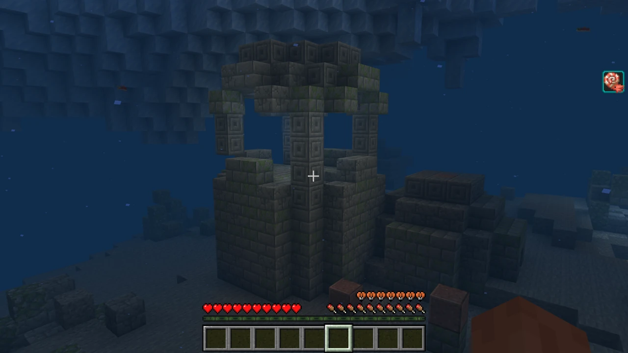 First-person view of a player exploring an elaborate Minecraft Ocean Ruin underwater, with full health and hunger, and a Heart of the Sea icon displayed.
